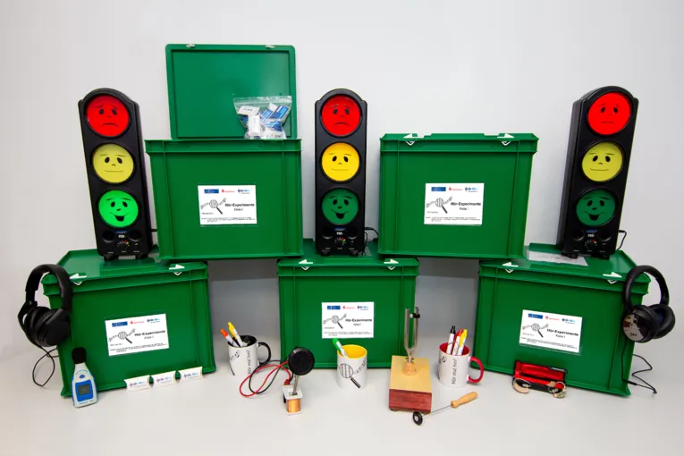 Grüne Kisten, deren Inhalt ausgepackt zu sehen ist - unter anderem Gehörschutz, eine Art Ampeln, Tassen, ein Lautstärkemessgerät und vieles mehr